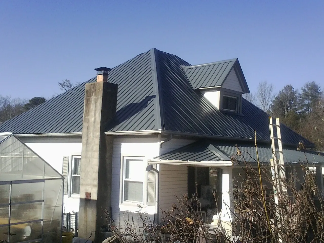 Dark blue standing seam metal roof on a white farmhouse with dormer — Slate & Tile Roof Repair by Roofing Brothers in Sharpsville