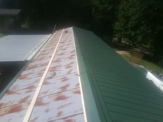 Old rusted panels beside newly installed green metal roofing — Wind Damage Roof Repair by Roofing Brothers in Sharpsville