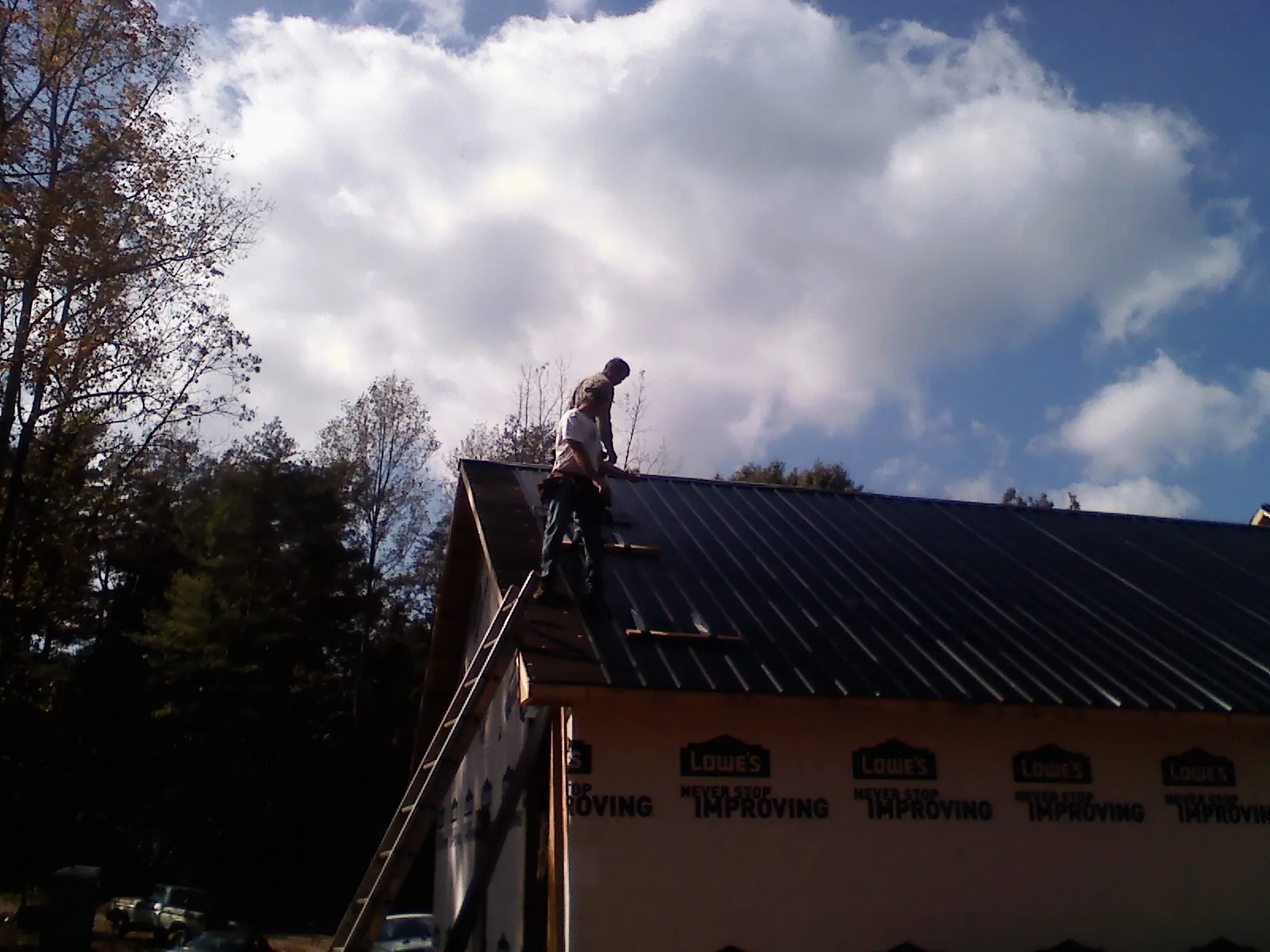 Roofer fastening dark metal panels high against a cloudy sky, from a Roof Inspection job in Sharpsville