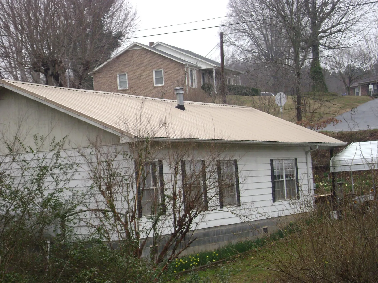 Tan metal roof on a white sided house set into a hillside — Commercial Roofing by Roofing Brothers in Sharpsville