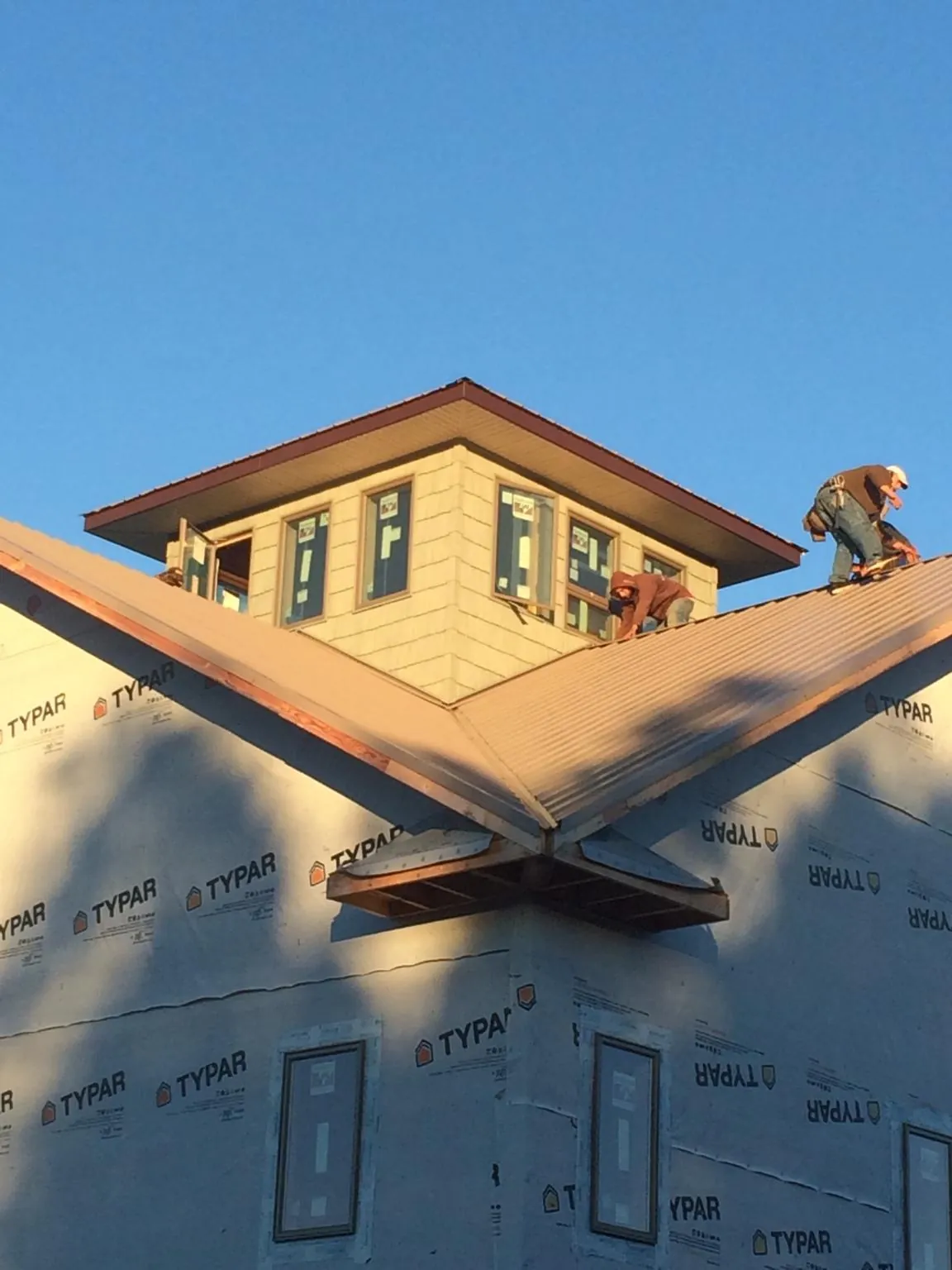 Roofers working around a rooftop cupola on a new metal roof at sunset in Sharpsville